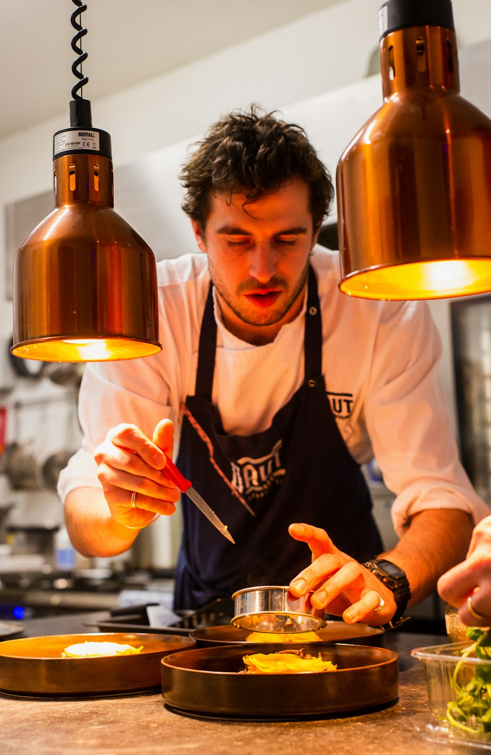 Chef plating a course under warm copper heat lamps